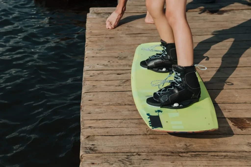 Rider ajustando bota wakeboard Liquid Force na beira do cable park antes de entrar na água