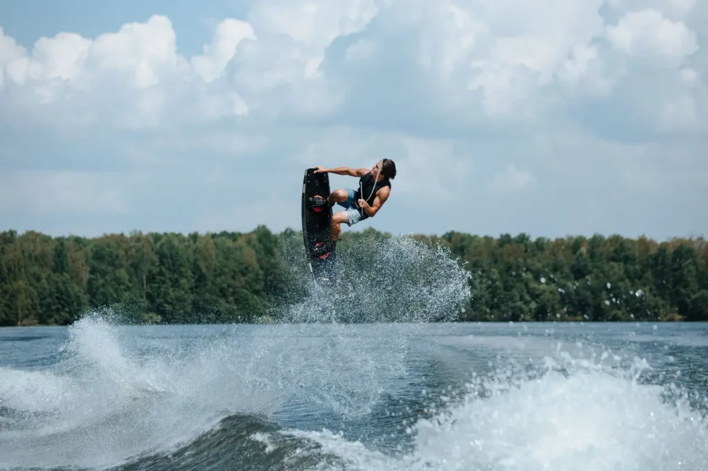 Rider em prancha de wakeboard Sea Doo sendo rebocado por jet ski em lago com água calma