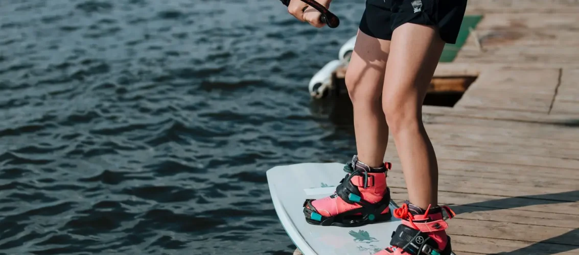 Rider ajustando a bota de wakeboard Ronix Anthem BOA no deck de um cable park antes de entrar na água
