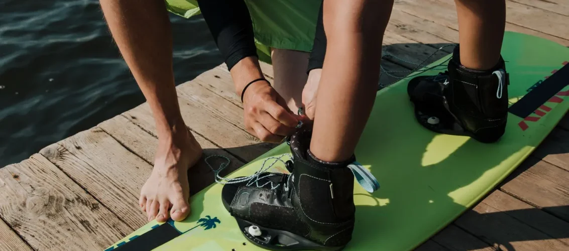 Criança ajustando a wakeboard bindung kids na beira do lago antes de entrar na água para praticar